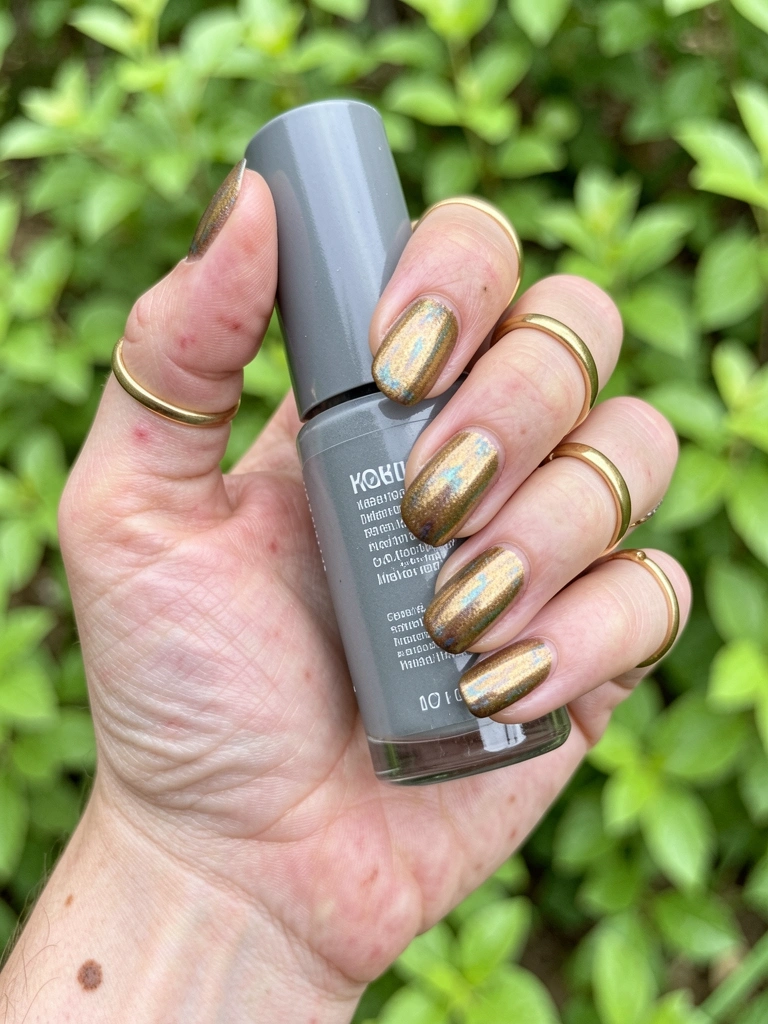 Mãos com esmalte dourado envelhecido e anéis dourados finos sobre superfície neutra