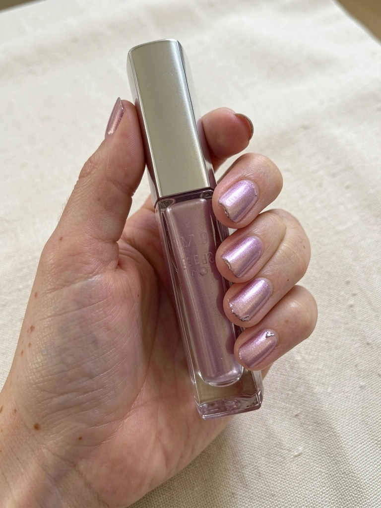Mão com unhas pintadas de rosa metálico claro apoiada sobre superfície bege lisa