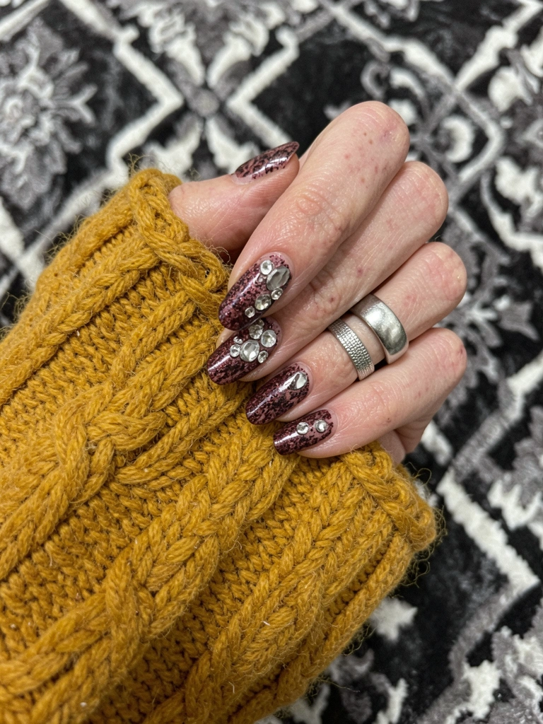 Mãos com unhas compridas em formato amendoado cobertas por glitter dourado sobre fundo neutro.